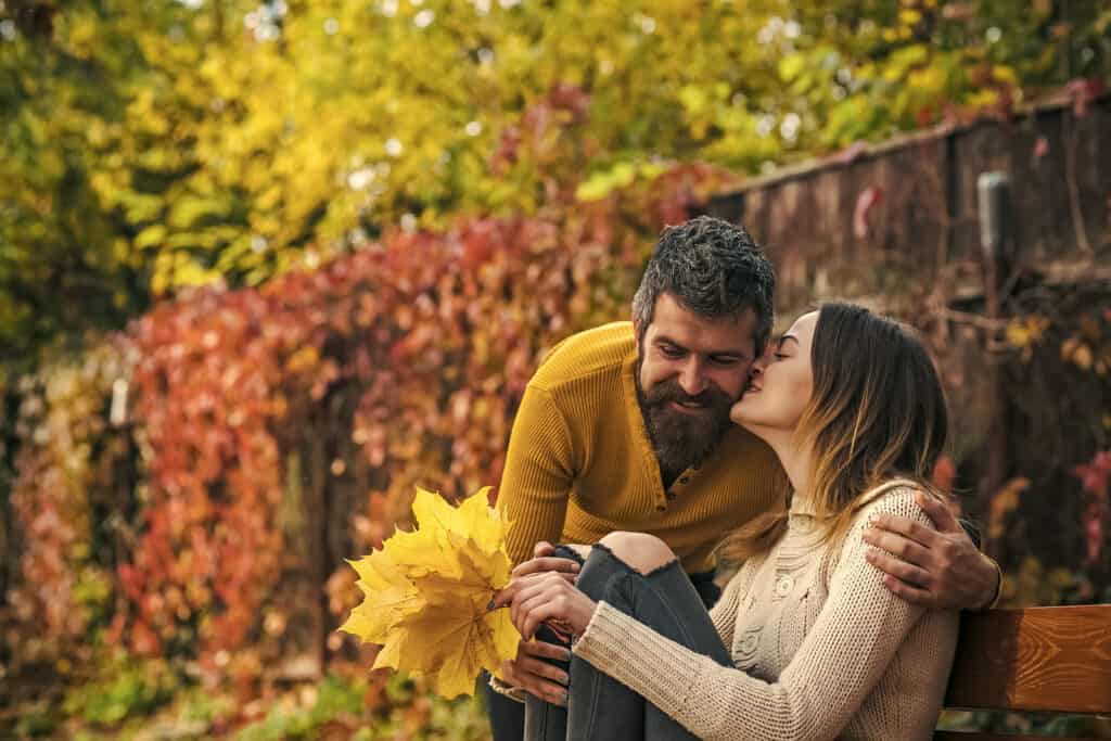 A couple kisses while holding big yellow leaves outdoors in fall