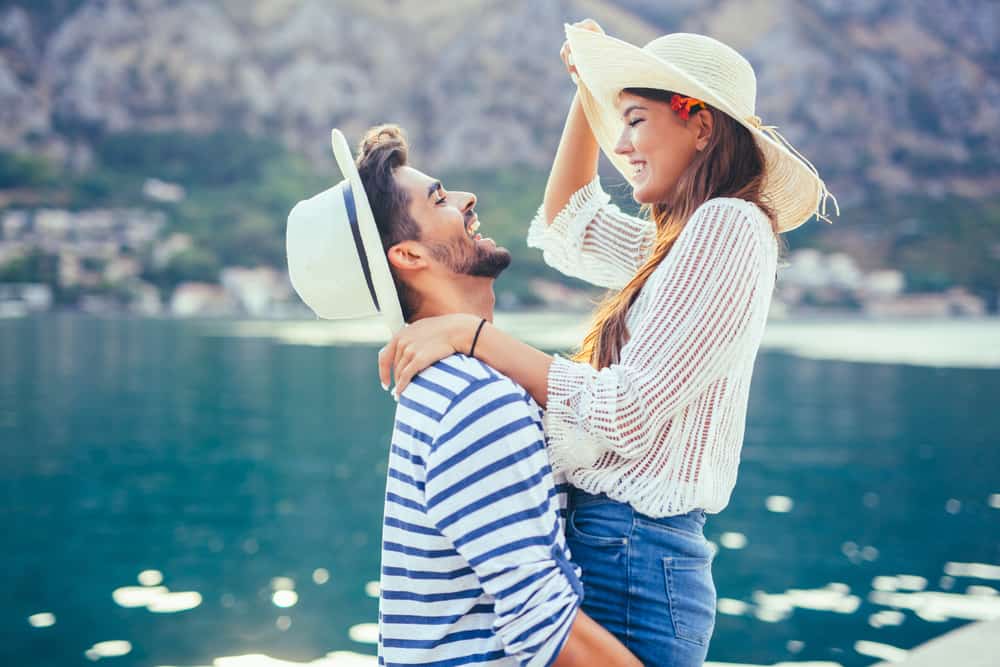 A couple embraces happily outdoors with hats on.