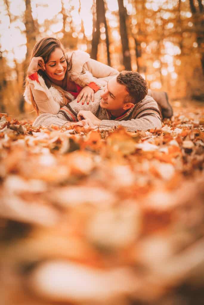 A couple lays on the forest floor in fall leaves.