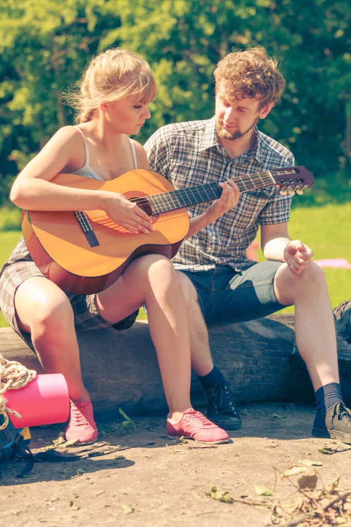 A woman plays a guitar while a man sits next to her listening.