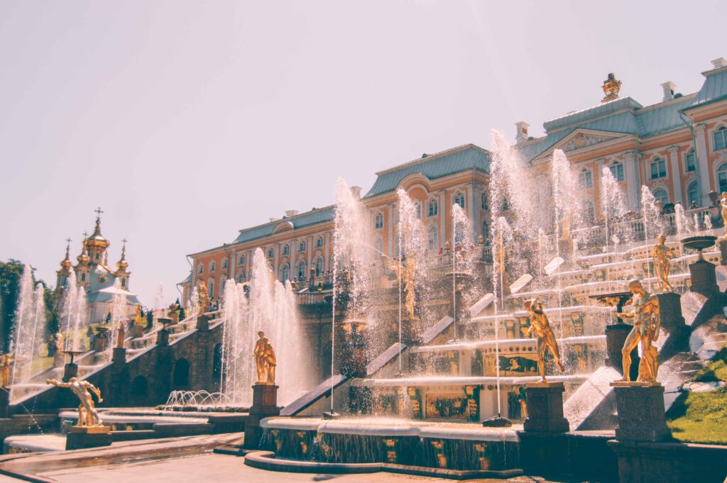 A large water feature with various gold statues throughout it in front of a large palace. 