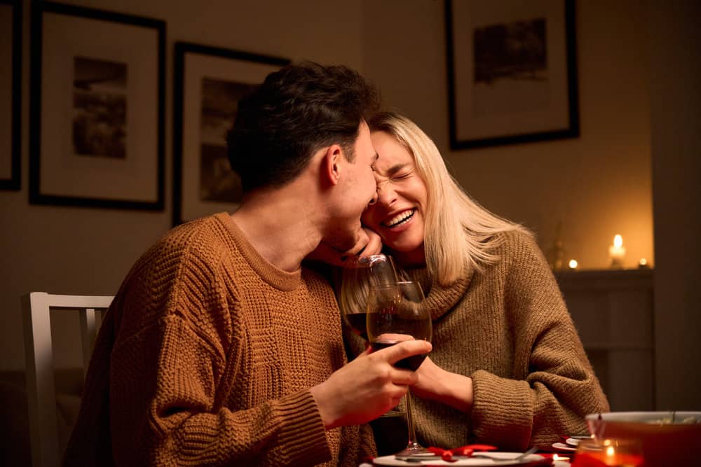 A couple laughs as they hold wine indoors.