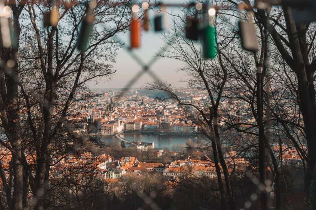 View through a fence of a town with red roofs surrounded by water.