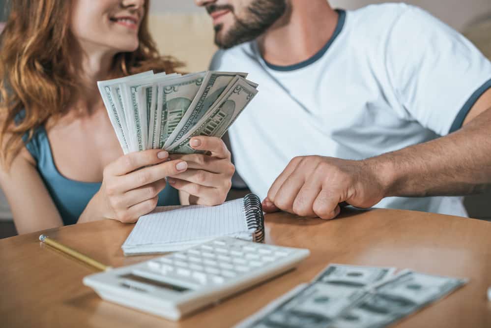 Man and woman hold money with a calculator.