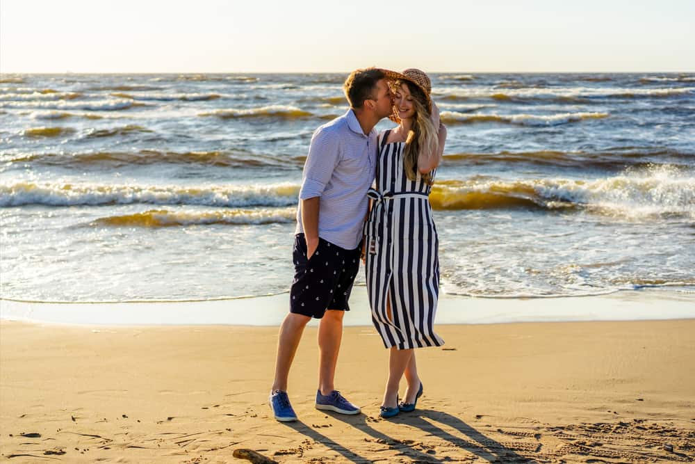 A man kisses a woman on the cheek while they stand on the beach.