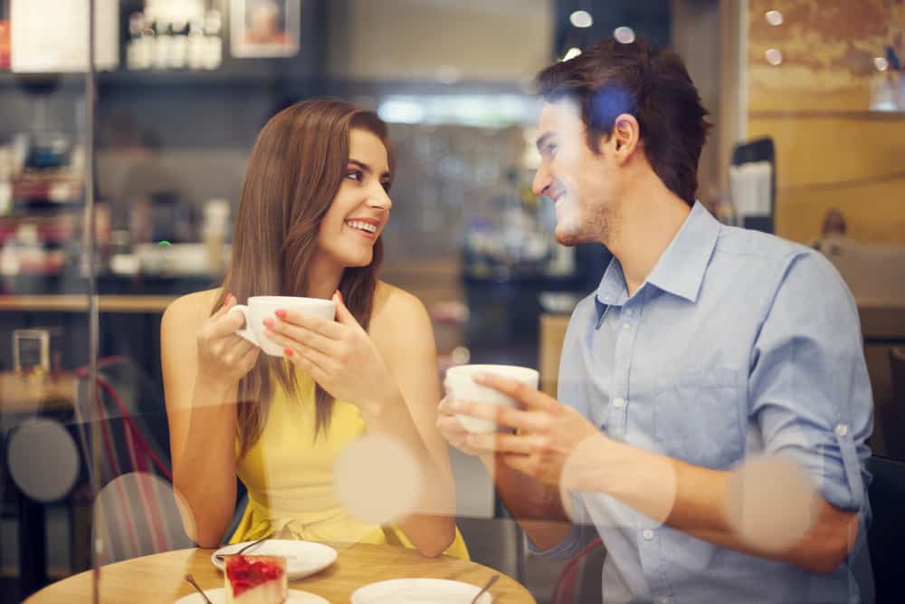 A couple on a date at a cafe, each holding a white mug.