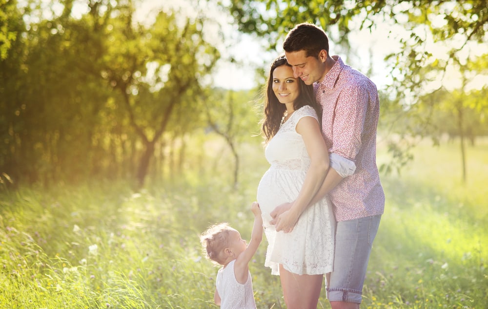 Man embraces a woman\'s stomach with a child in front of them.