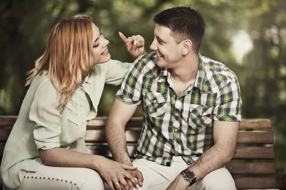 A man and woman laugh while chatting with each other on a bench.