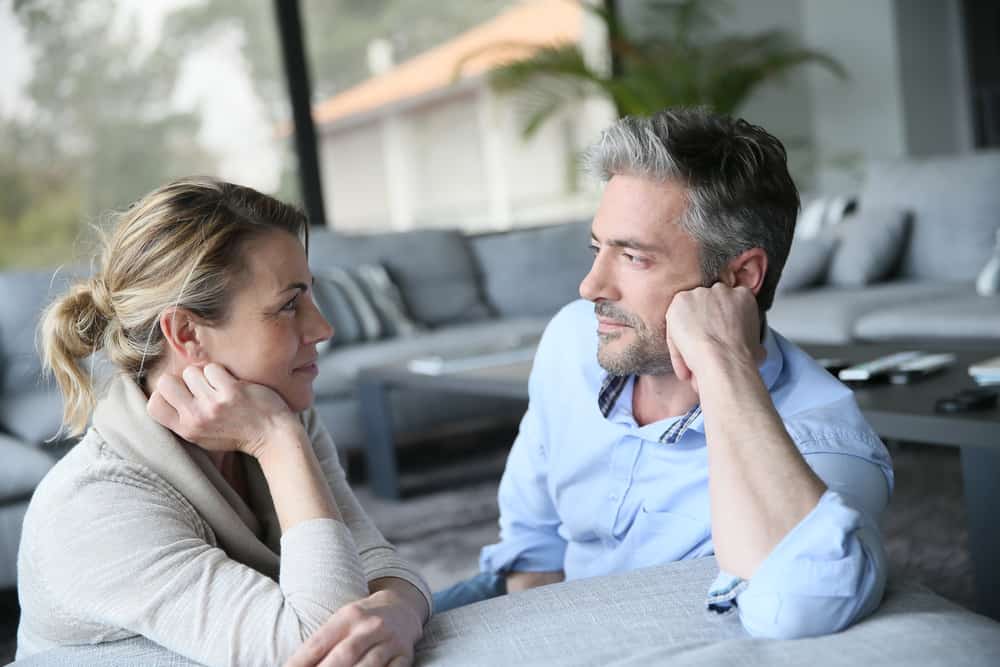 A man and woman look at each other with their hands on their head.