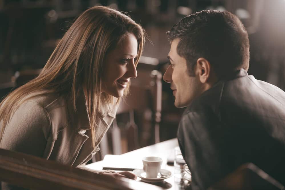 A couple sits staring at one another\'s eyes in a bar.