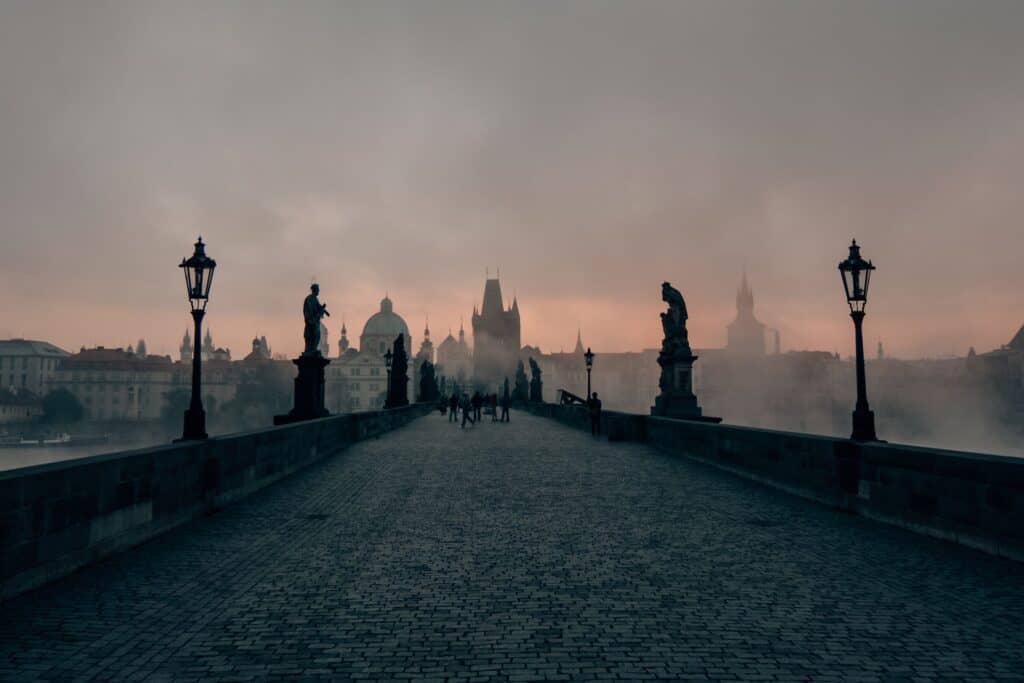 People walking on a bridge lined by statues with a hazy background.