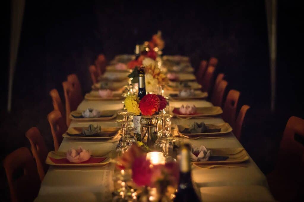 A long table candlelit and made with a table cloth and place settings.