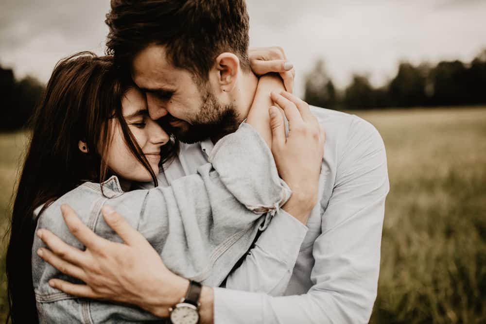 A man and woman embrace one another in a field.