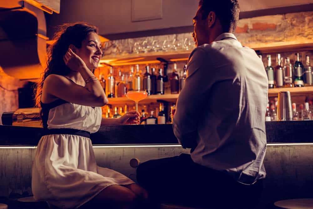 A man and woman talk at a bar and flirt.