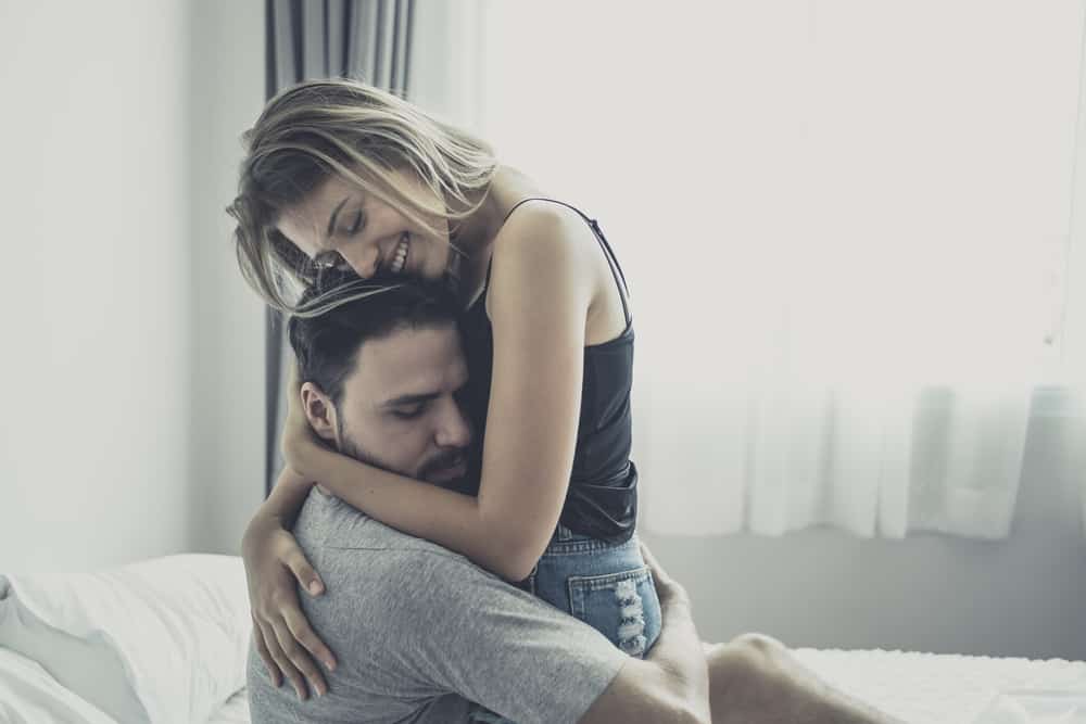 A happy couple is smiling and hugging each other in a bed with a hazy background.