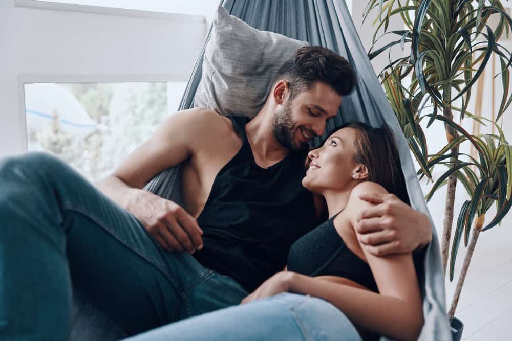 A couple lays together in a hammock. They look at each other and smile.