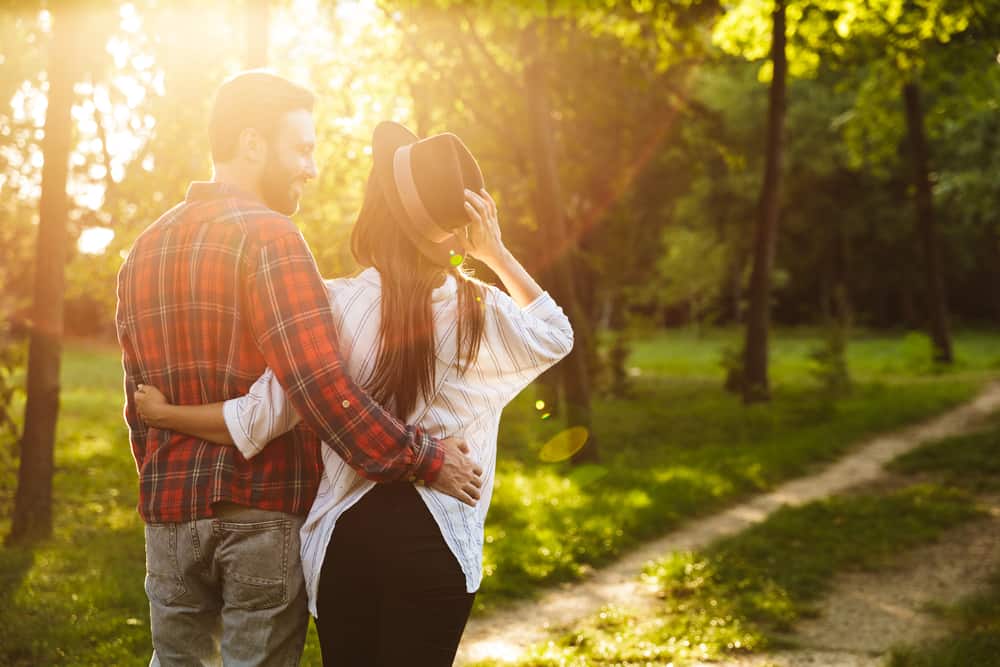 A couple embraces each other while walking in a forest.