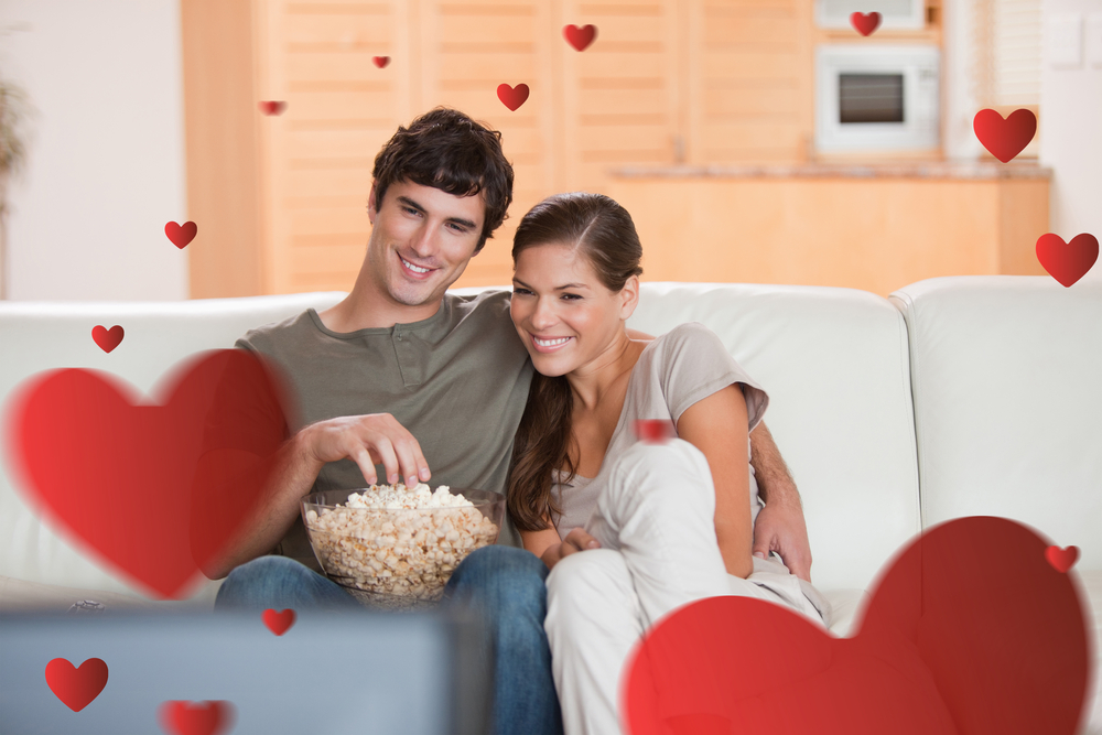 Couple with popcorn on the sofa watching a movie against hearts