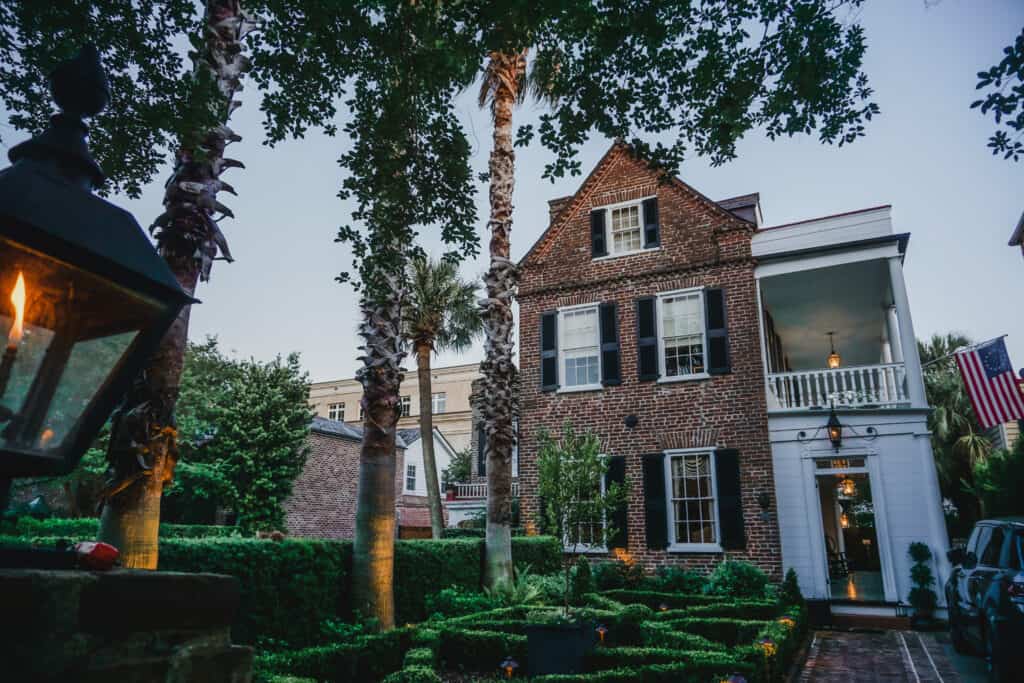 A historic brick home stands tall with trees and a garden in front.