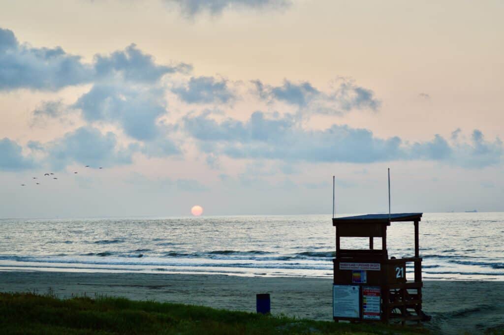 A calm beach with the sun low in the sky in the distance.