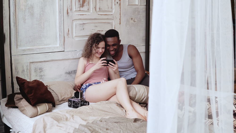 A couple sits while looking at a phone that the woman holds.