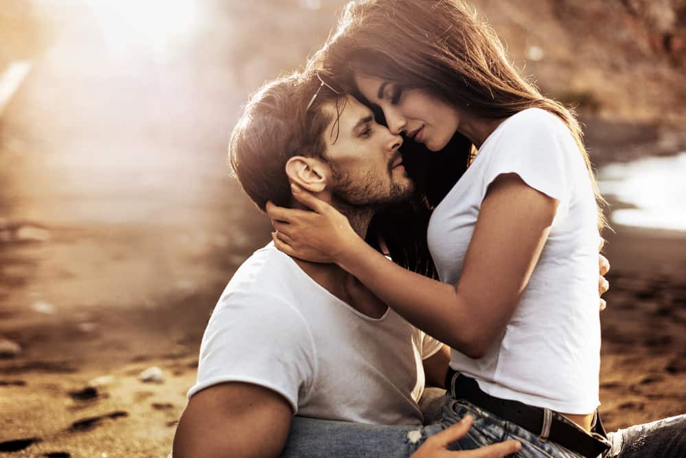 A couple is embraced while sitting outdoors. They are both in white t shirts.