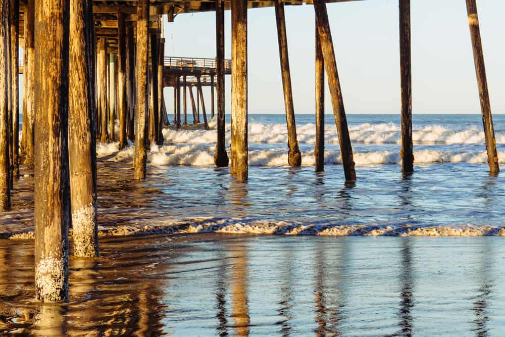 Waves crash against the beach underneath a wooden pier.