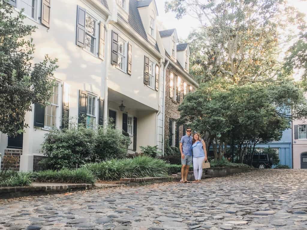 A couple embraces one another while walking on a stone walkway next to a historic white building.
