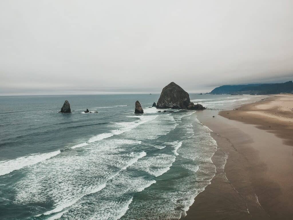 Waves crash against the sand with tall rocks in the beach.