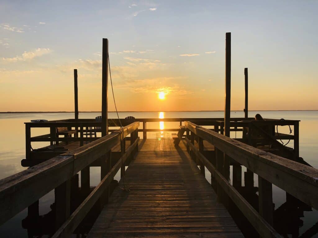 An empty wooden pier leading out to the ocean while the sun sets in the distance.