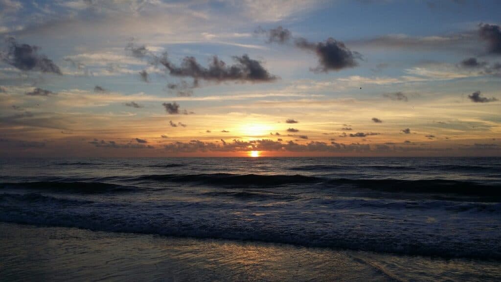 Waves crash in the orange with the sun sets in the background.