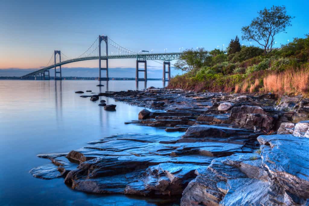 A bridge stretches across the ocean under a blue and orange sky.