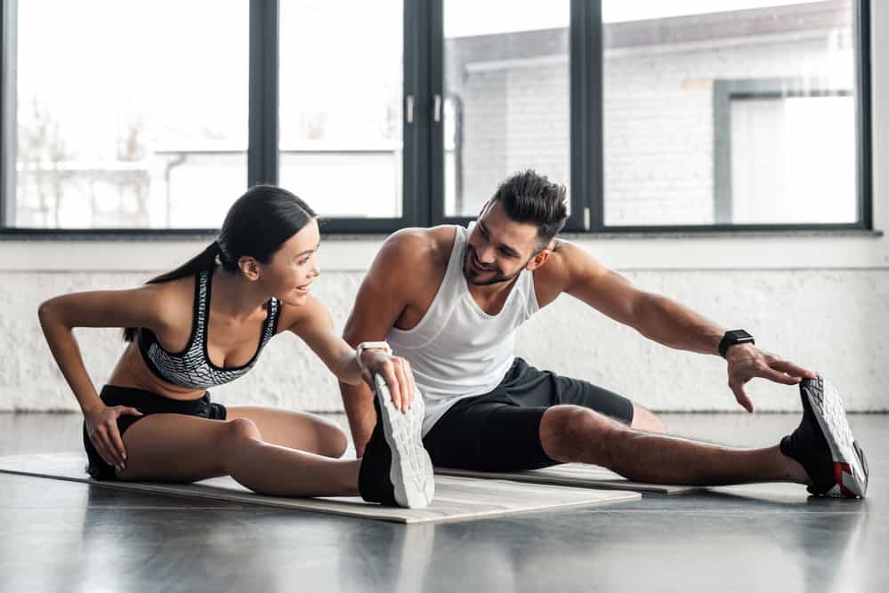 A couple leans over and stretches while doing a workout.