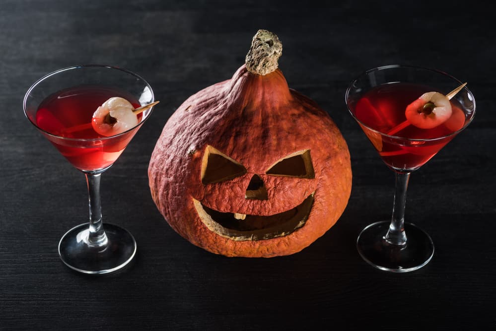 Close up of orange pumpkin holding a red cocktail glass on either side.