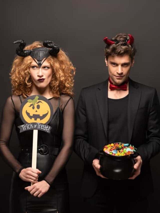 A couple in Halloween costumes poses with a black wall behind them.