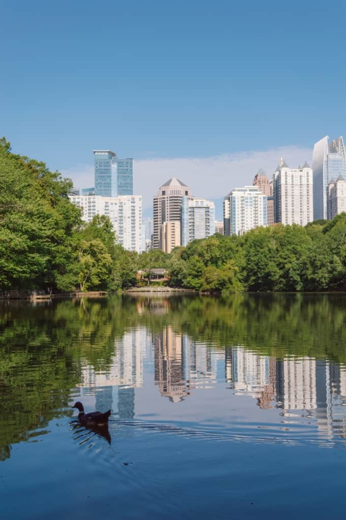 A city skyline is in the background while a lake surrounded by greenery is in the foreground.