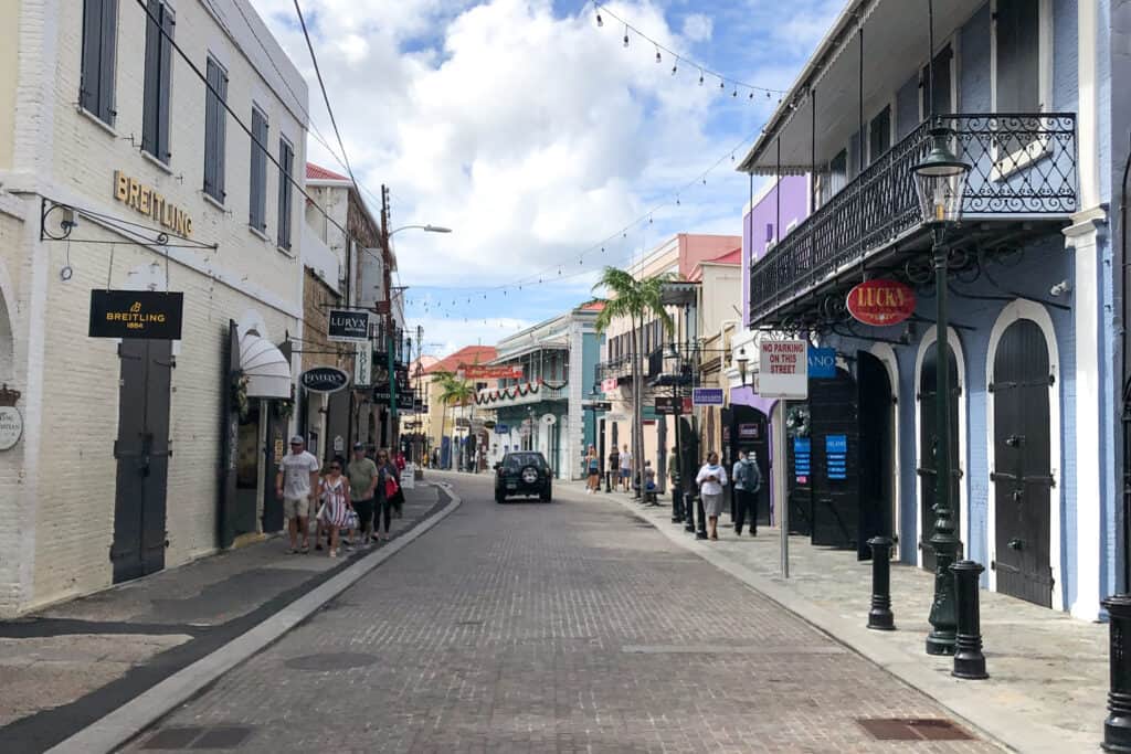 People walk along a street lined with shops of pastel colors.