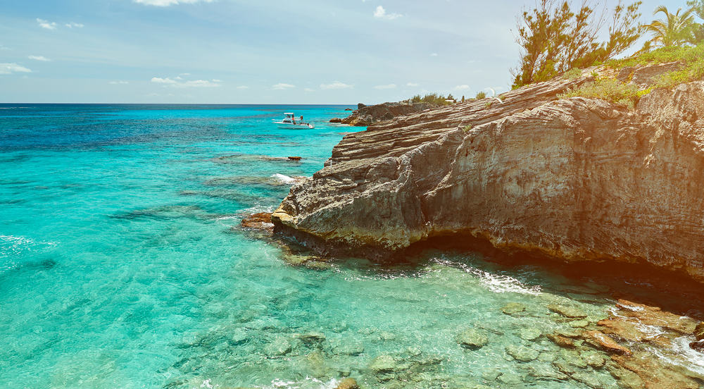 A boat floats in the water next to a rocky coast.