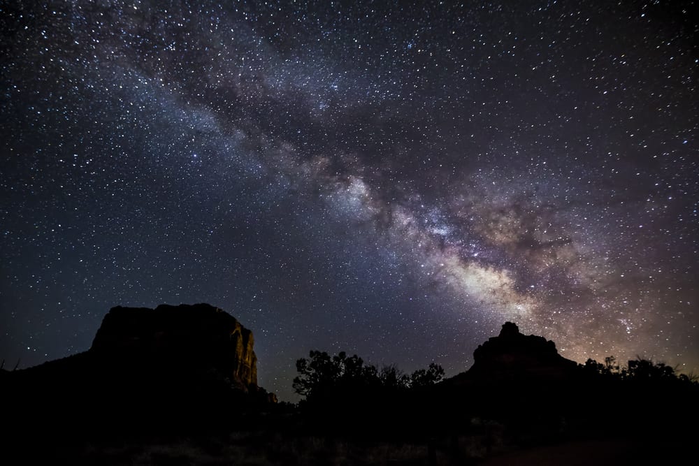 The Milky Way Galaxy arcs across the sky from Bell Rock over Courthouse Butte on a dark night near Sedona, Arizona.