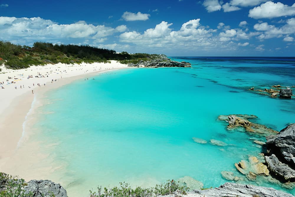 People in the distance relax along the beach surrounded by bright blue water.