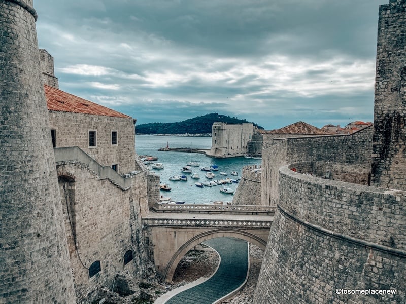 Tall stone fortress next to an ocean with boats floating on it.