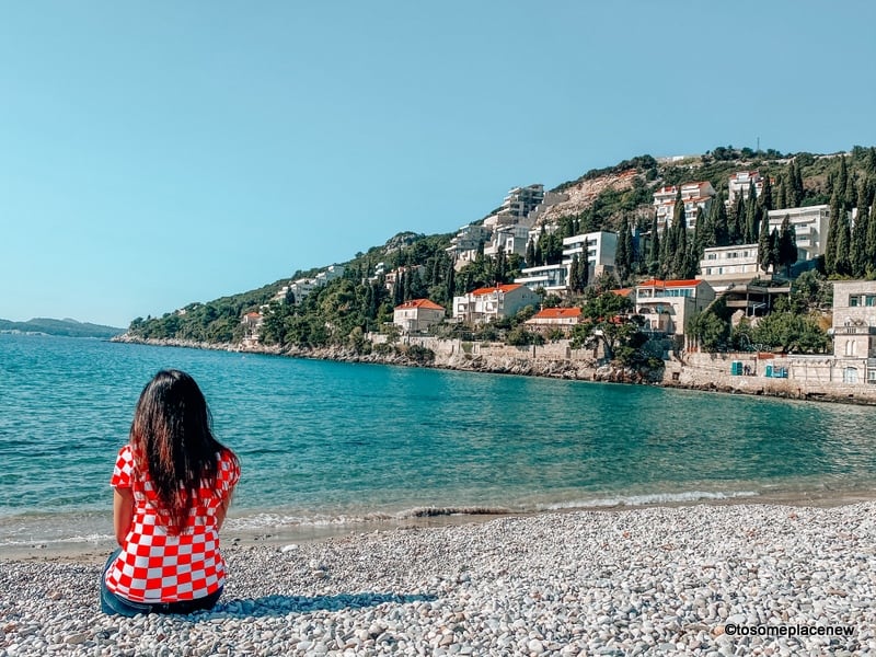 A woman sits on the beach looking out at the water.