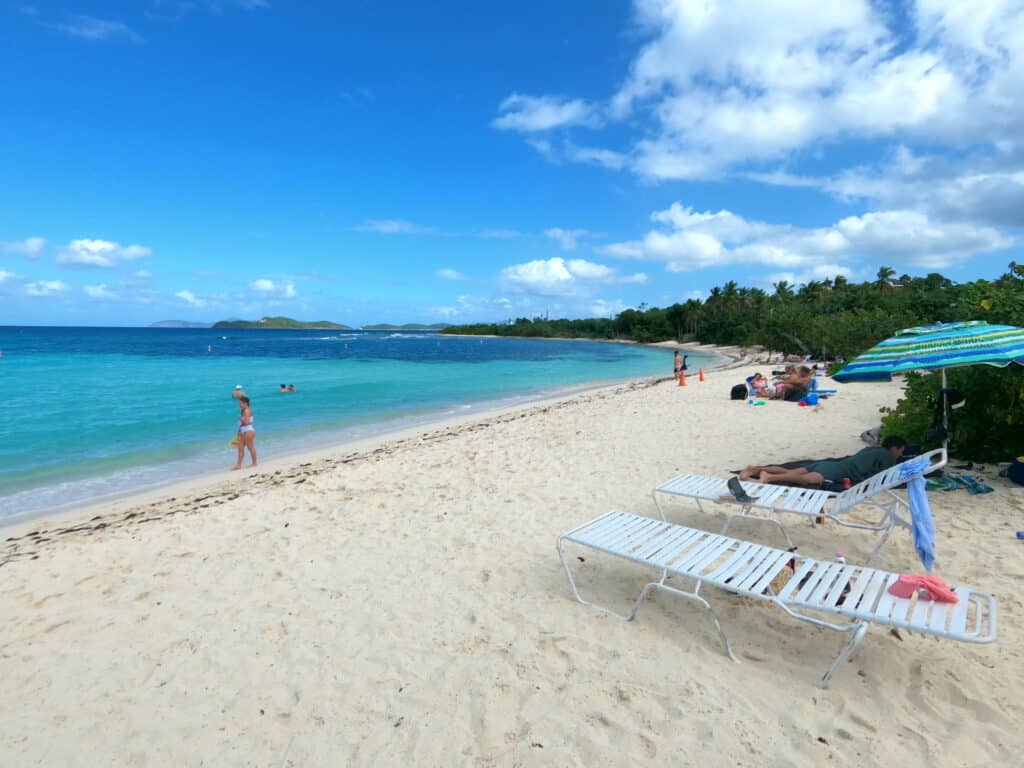 Tourists relax on white chairs along the beach.