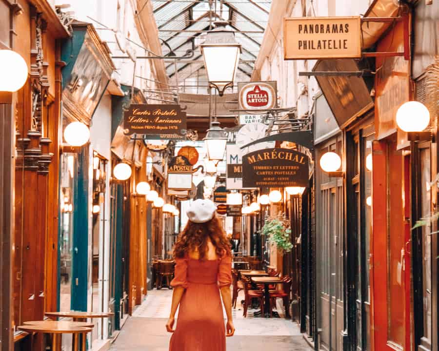 A woman walks through a small alley lined with shops.