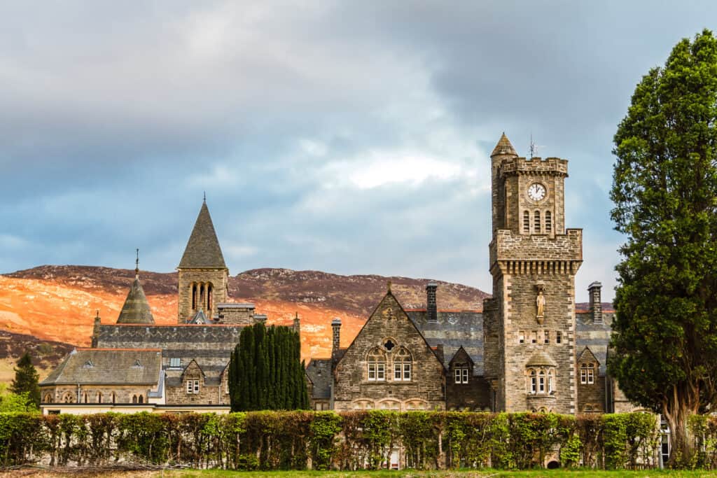 A historic building with a clock tower stands tall next to a mountain under a grey sky.