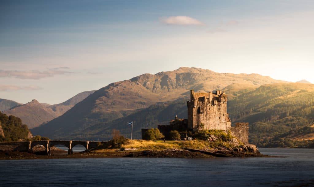 A historic castle sits on an island with a large mountain behind surrounded by water.