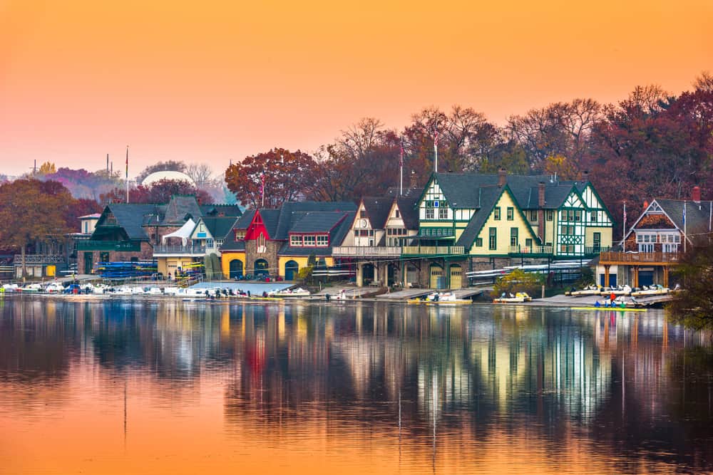 The sun sets over colorful historic homes along the water, casting an orange glow.