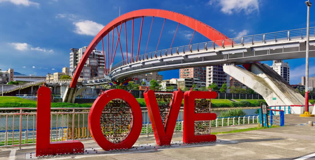 A big red sign says LOVE next to the water. Behind it, a bridge crosses the water.