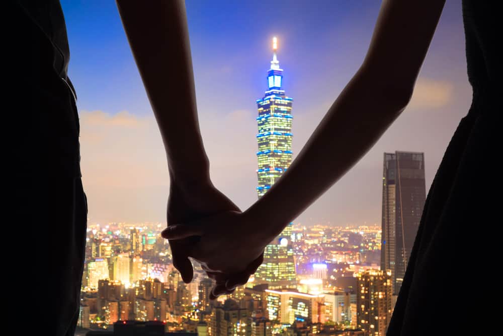A couple holds hands in front of a city skyline at night