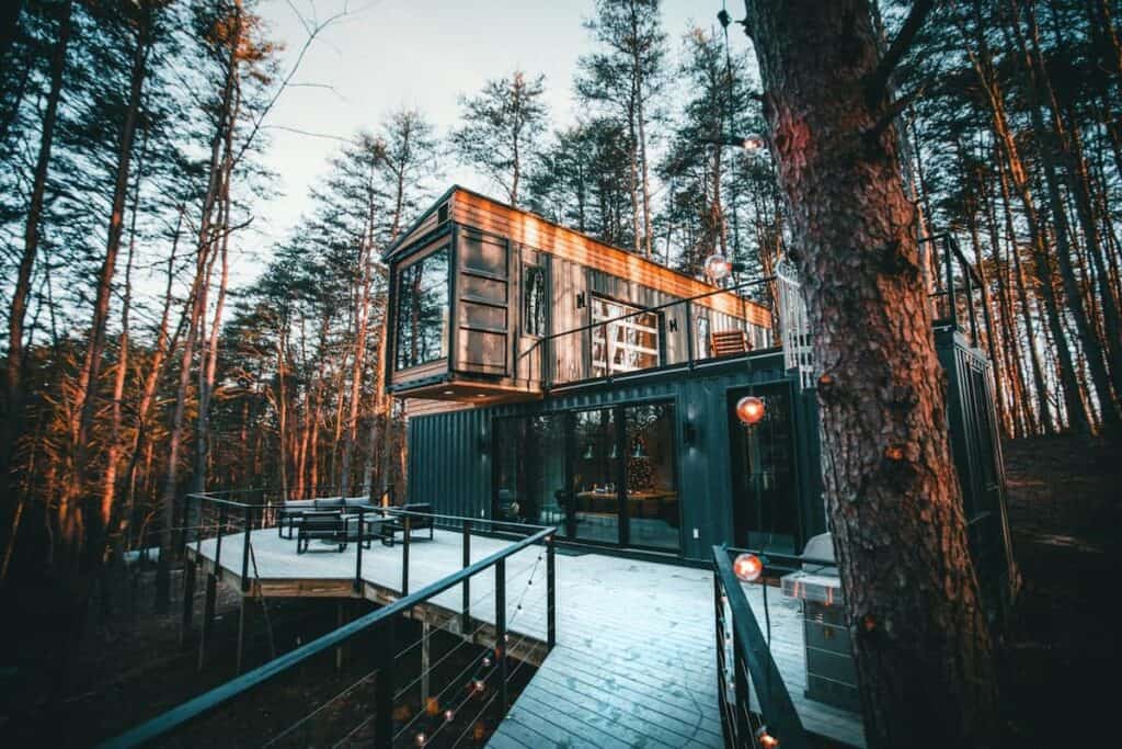 Industrial-style vacation home with a walkway leading to it, surrounded by trees.